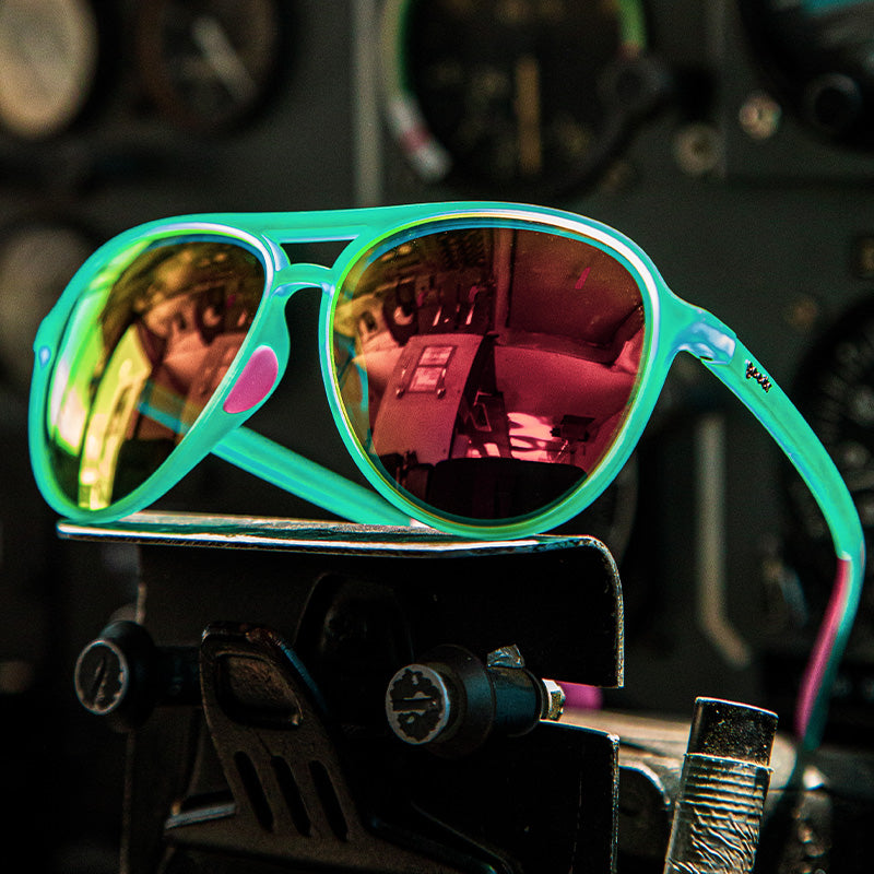 Three-quarter angle view of teal aviator sunglasses with pink mirrored lenses sitting atop metal gym equipment.
